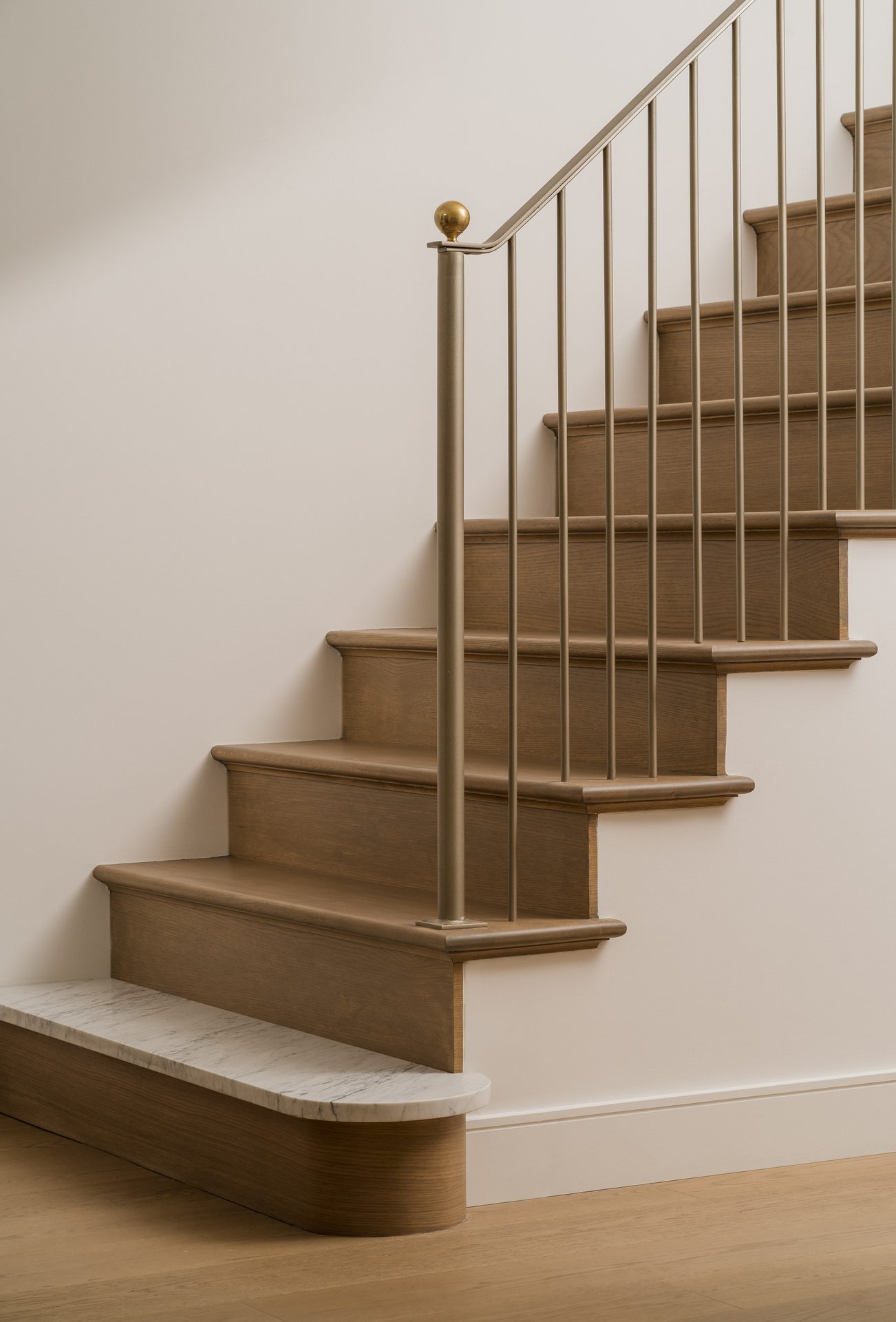 A staircase detail where wood treads meet a marble step, brass hardware at the newel post
