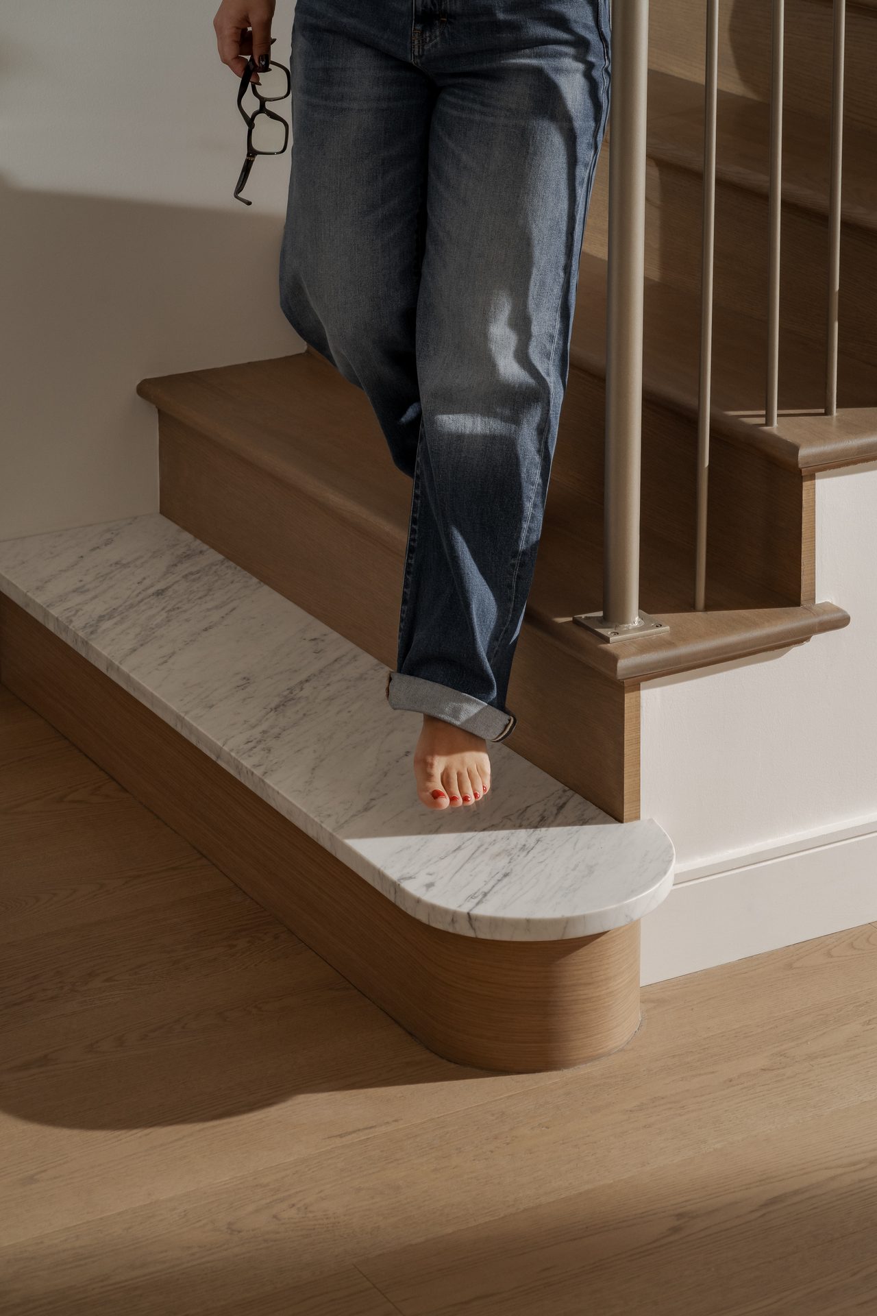 Bare feet on a staircase where marble meets wood, brass hardware at the newel post